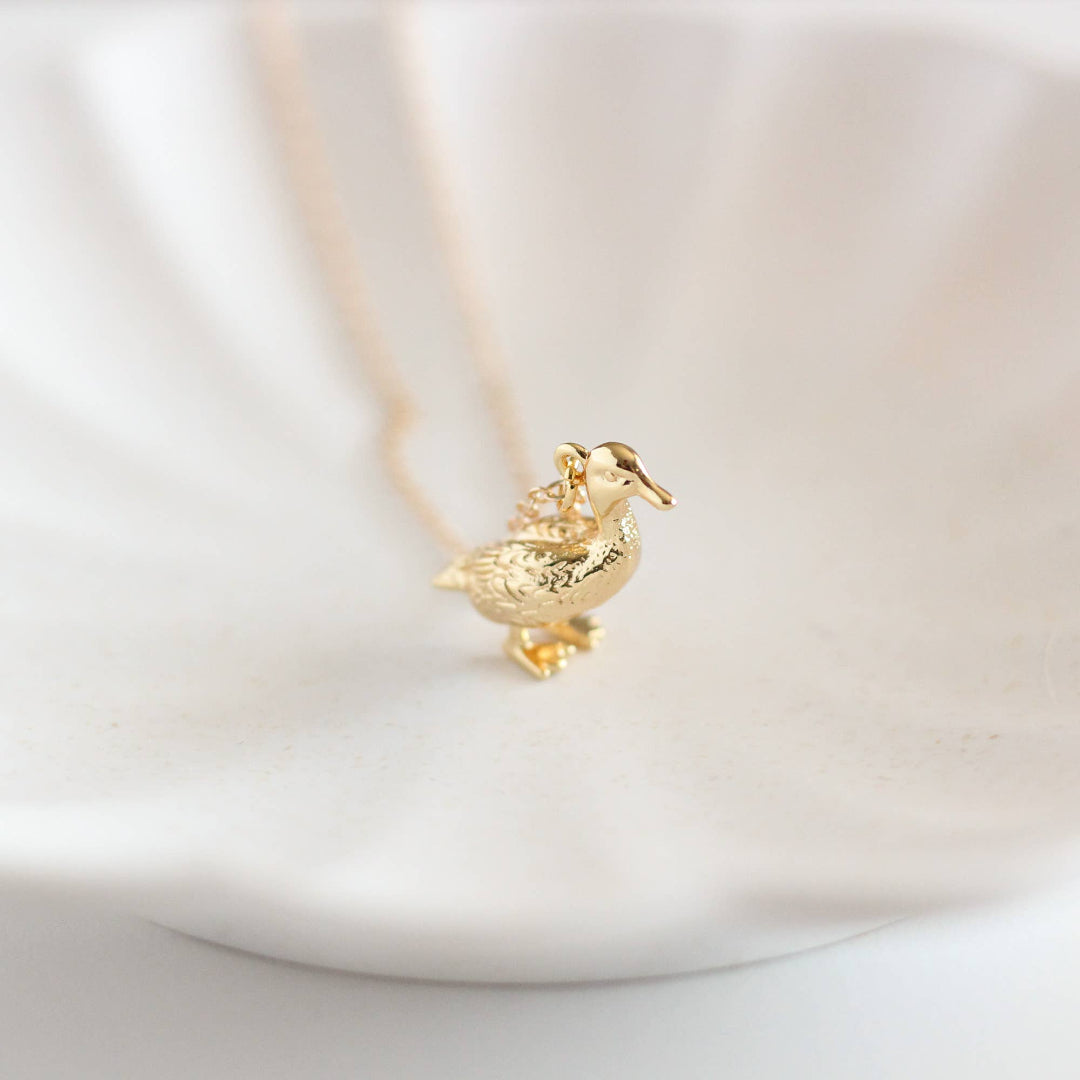 Gold duck-shaped pendant on a chain against a light background
