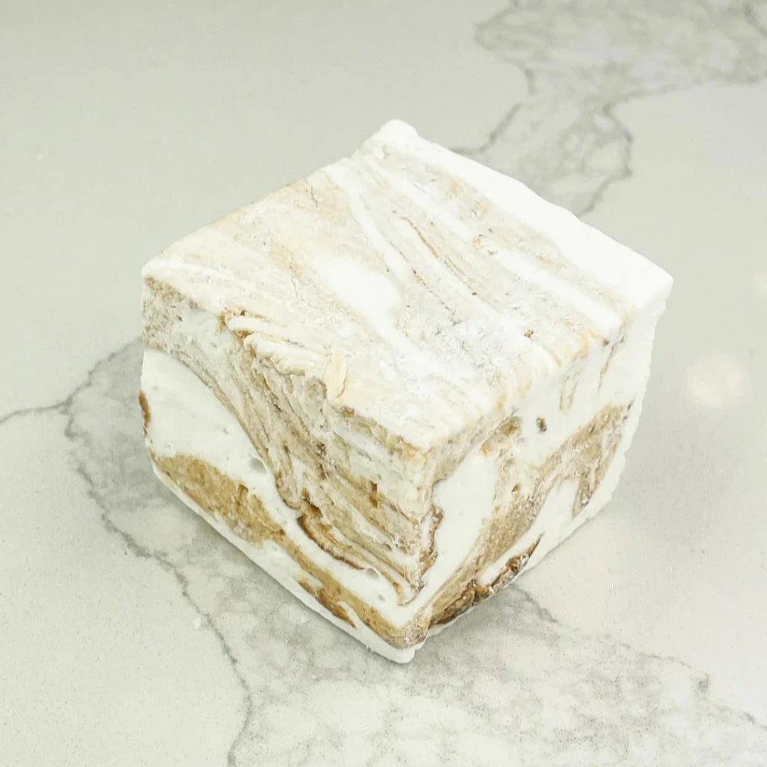 A square marshmallow with swirls of white and brown. The marshmallow is resting on a white marble surface.