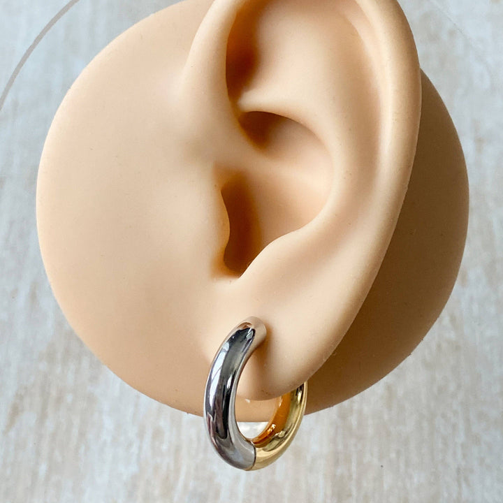 Two-tone chunky hoop huggie earrings (gold and silver) by agaveh girl, displayed on a branded card with the text 'agaveh girl,' against a textured background. The earrings are 4mm thick, made of stainless steel, and are sold in Ottawa, Ontario, Canada