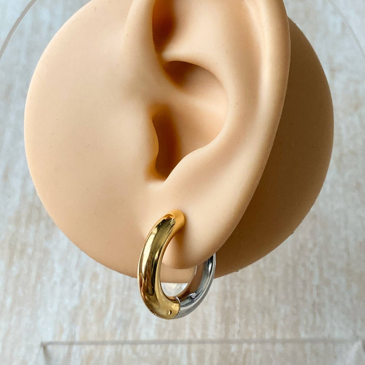 Two-tone chunky hoop huggie earrings (gold and silver) by agaveh girl, displayed on a branded card with the text 'agaveh girl,' against a textured background. The earrings are 4mm thick, made of stainless steel, and are sold in Ottawa, Ontario, Canada