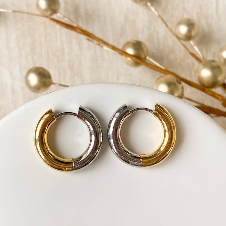 Two-tone chunky hoop huggie earrings (gold and silver) by agaveh girl, displayed on a branded card with the text 'agaveh girl,' against a textured background. The earrings are 4mm thick, made of stainless steel, and are sold in Ottawa, Ontario, Canada