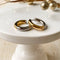 Two-tone chunky hoop huggie earrings (gold and silver) by agaveh girl, displayed on a branded card with the text 'agaveh girl,' against a textured background. The earrings are 4mm thick, made of stainless steel, and are sold in Ottawa, Ontario, Canada
