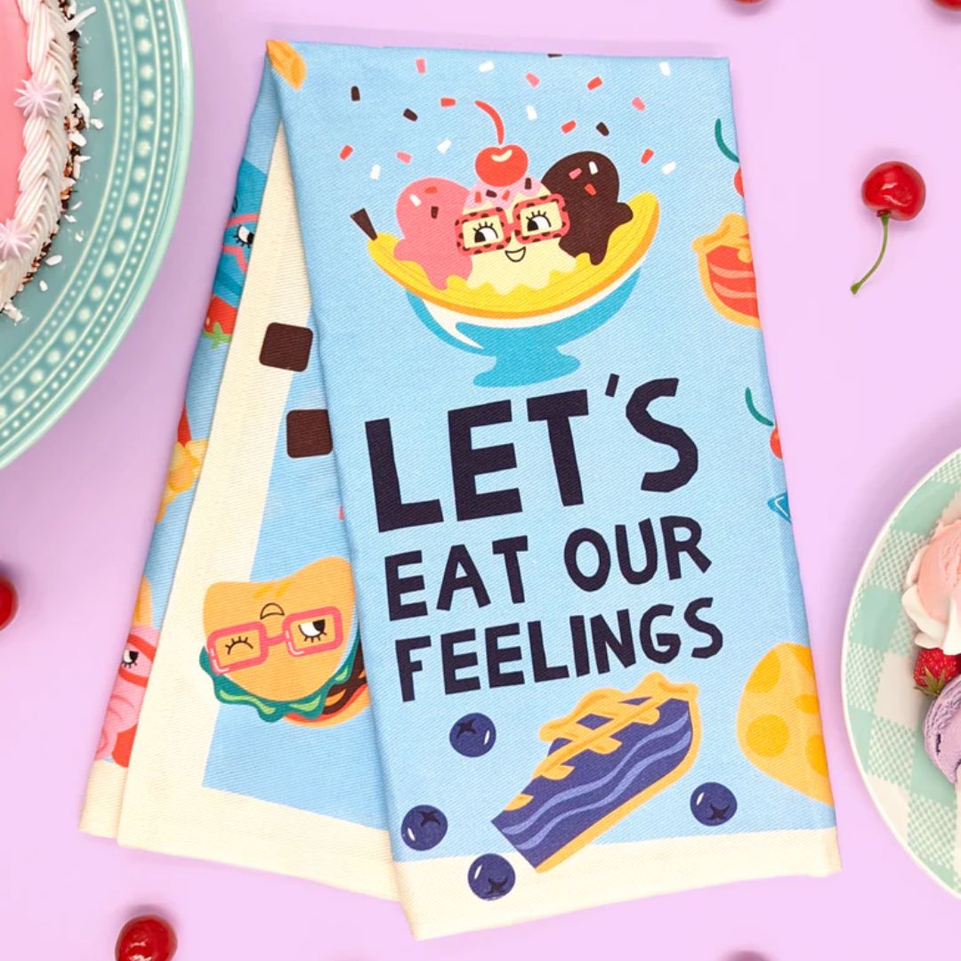 Colorful towel with cartoon characters and 'Let's Eat Our Feelings' text on a pink background with cherries.