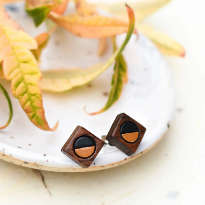 A pair of wooden earrings shaped like squares with half of each earring painted black and the other half a lighter color.
