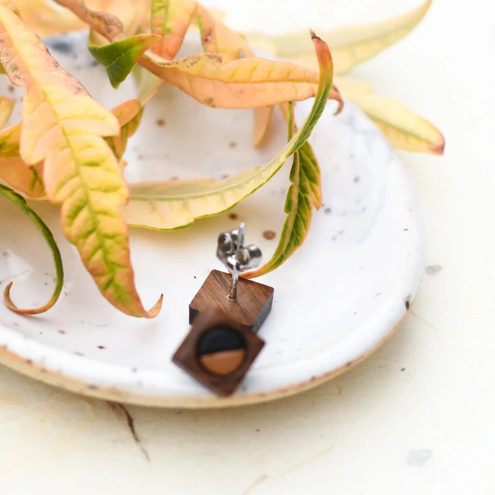 A pair of wooden earrings shaped like squares with half of each earring painted black and the other half a lighter color.