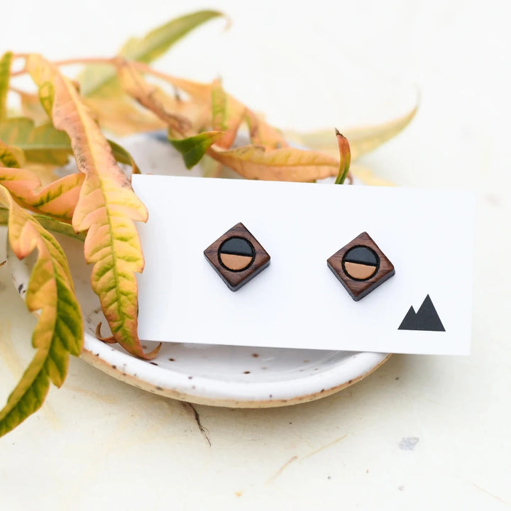 A pair of wooden earrings shaped like squares with half of each earring painted black and the other half a lighter color.