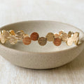 A gold-toned bangle bracelet with a row of circular discs. 