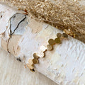 A gold-toned bangle bracelet with a row of circular discs. 