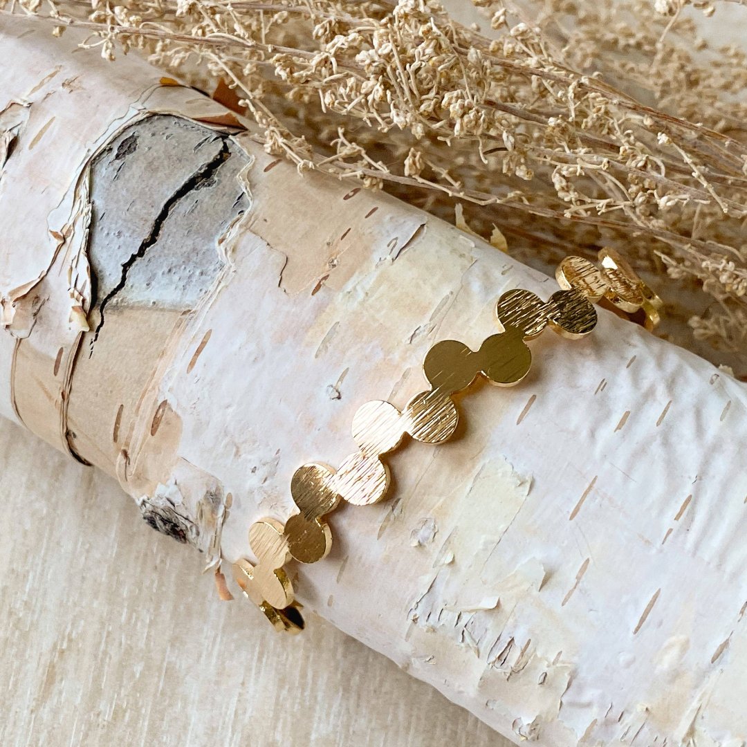 A gold-toned bangle bracelet with a row of circular discs. 