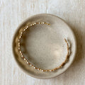 A gold-toned bangle bracelet with a row of circular discs. 