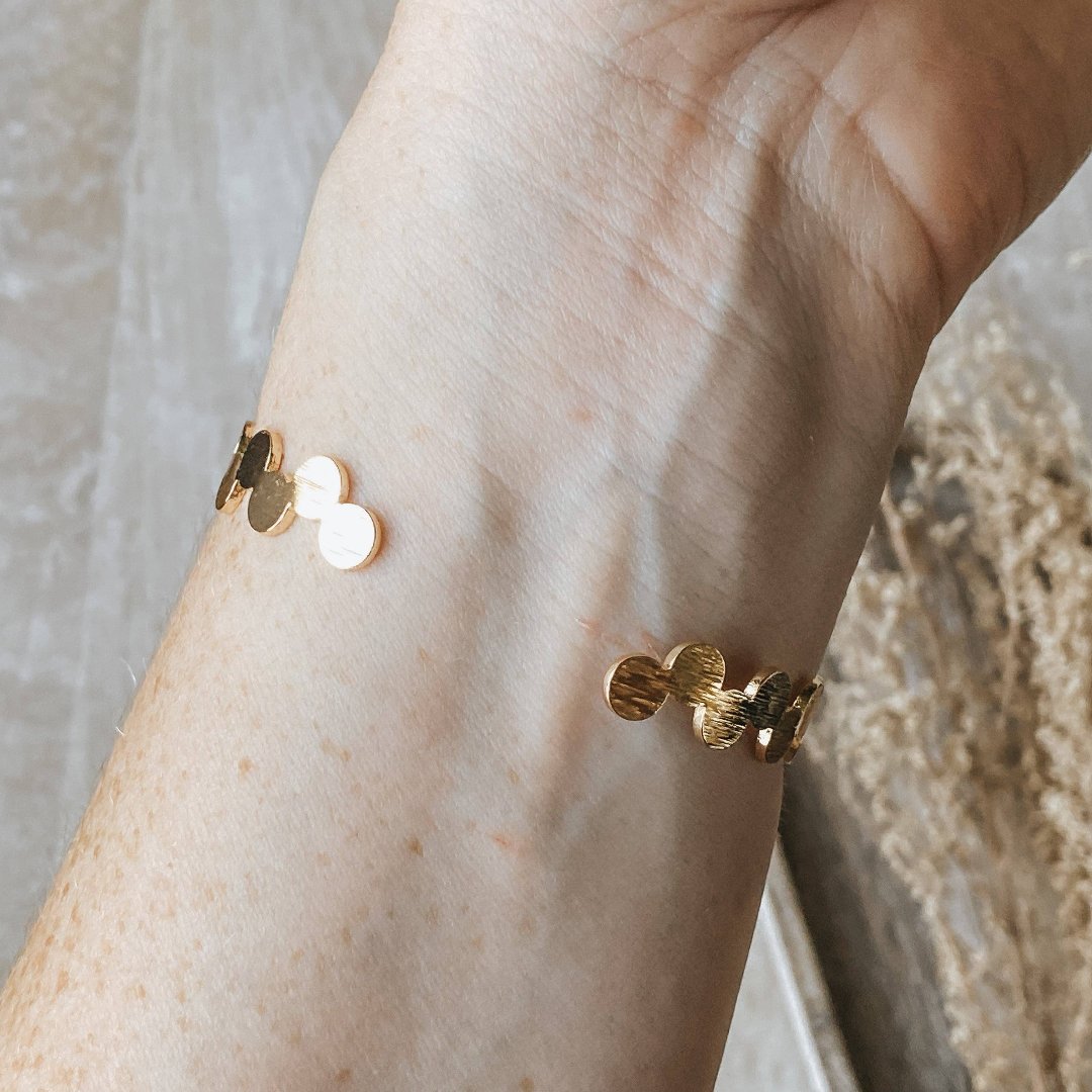 A gold-toned bangle bracelet with a row of circular discs. 