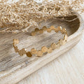 A gold-toned bangle bracelet with a row of circular discs. 