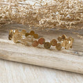A gold-toned bangle bracelet with a row of circular discs. 