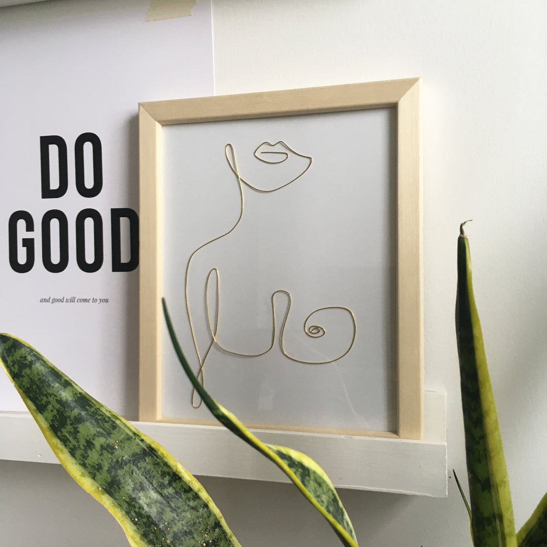 Framed minimalist line art of a woman's silhouette on a wall with motivational quote