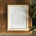 Framed line art of a cat on a textured surface with a plant in the corner