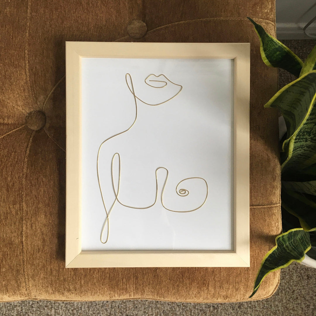 Framed line art of a cat on a textured surface with a plant in the corner