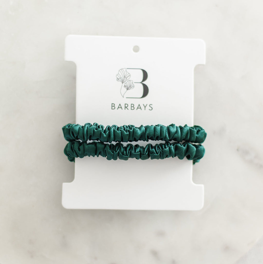 Two green scrunchies on a Barbays branded card against a marble background