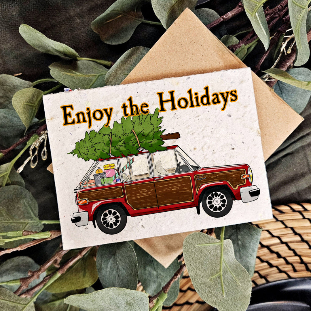 A card with the illustration of a old hatchback car with wood paneling with presents in the back and a tree strapped to the roof and the words "ENjoy the holidays"