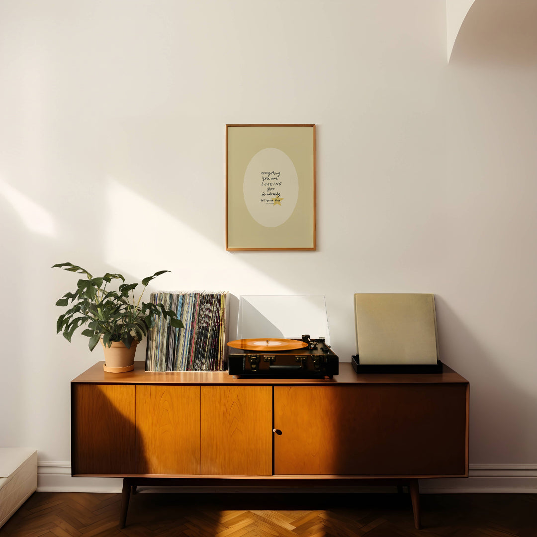 Wooden sideboard with vinyl records and a plant in a room with a framed picture on the wall.