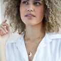 A gold necklace with an amethyst stone pendant. The pendant also has the word "WISDOM" engraved on it. The necklace is displayed on a purple card with the month "February" and the brand name "Foxy Originals."