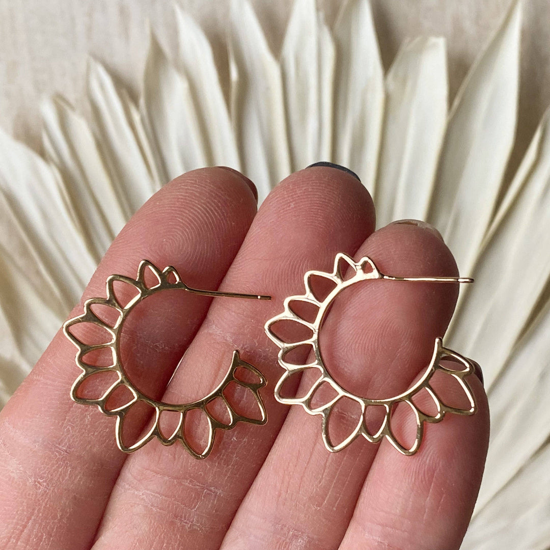 Gold hoop earrings held between fingers with a neutral background