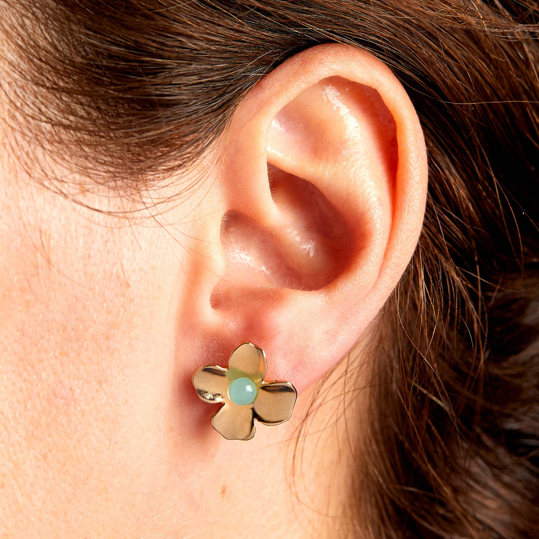 Gold flower-shaped earring with a green gemstone worn by a person.