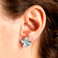 Silver flower-shaped earring worn on an ear with a blurred background