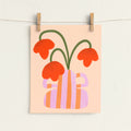 A minimalist art print featuring orange flowers in a pink and orange striped vase, hanging from a string with wooden clothespins against a textured off-white wall.