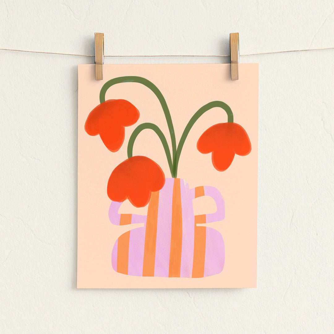A minimalist art print featuring orange flowers in a pink and orange striped vase, hanging from a string with wooden clothespins against a textured off-white wall.