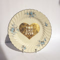 Decorative plate with floral designs and a gold heart with text on a white background