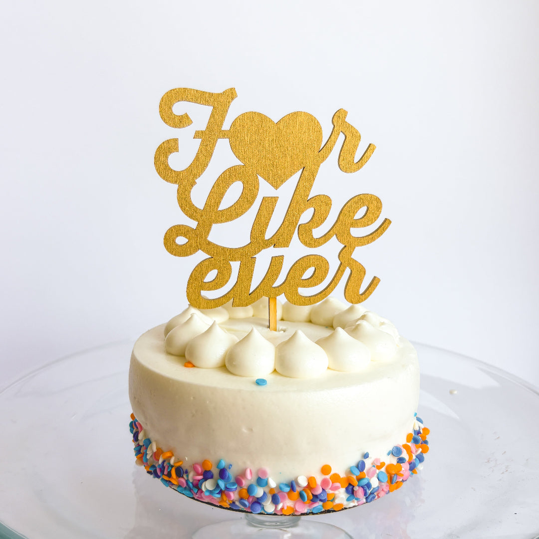 White cake with colorful sprinkles and a gold 'I love you like ever' topper on a white background