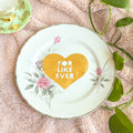 Decorative plate with a heart and floral design on a soft pink surface with leaves.