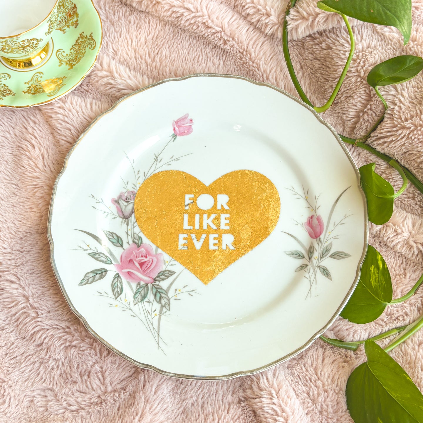 Decorative plate with a heart and floral design on a soft pink surface with leaves.