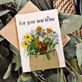 Greeting card with floral design and 'For your new home' text, surrounded by greenery.