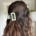 Close-up of a person's hair with a green hair clip, blurred background