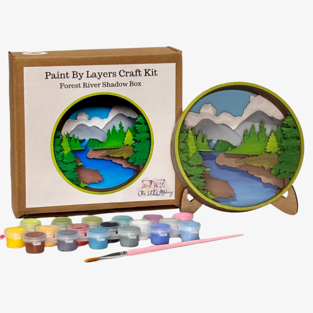 Paint by Layers Craft Kit with a completed forest river shadow box and paint supplies on a white background.