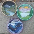 Three circular artworks depicting nature scenes on a concrete surface.