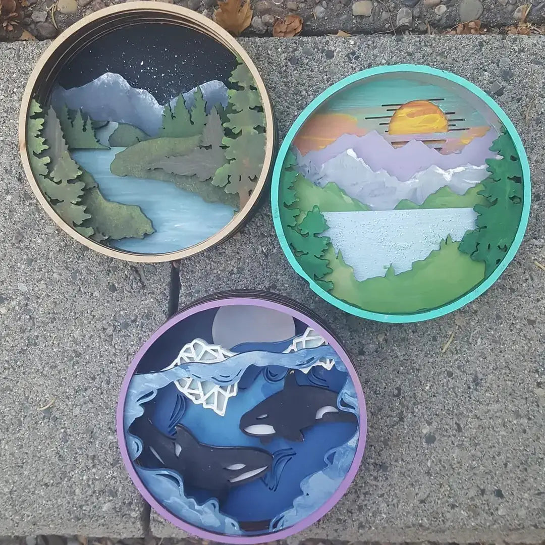 Three circular artworks depicting nature scenes on a concrete surface.