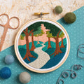 Embroidery hoop with a nature-themed design on a textured surface with sewing tools.