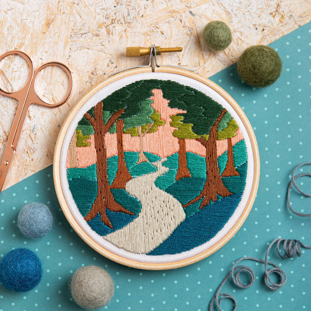 Embroidery hoop with a nature-themed design on a textured surface with sewing tools.