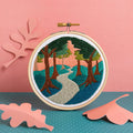 Embroidery hoop with a nature-themed design on a pink and blue background