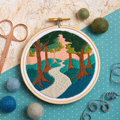 Embroidery hoop with a nature-themed design on a textured surface with sewing tools.