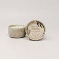 Speckled ceramic candle with decorative label on a light gray background