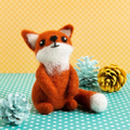 Felted fox toy on a polka dot surface with decorative pine cones.
