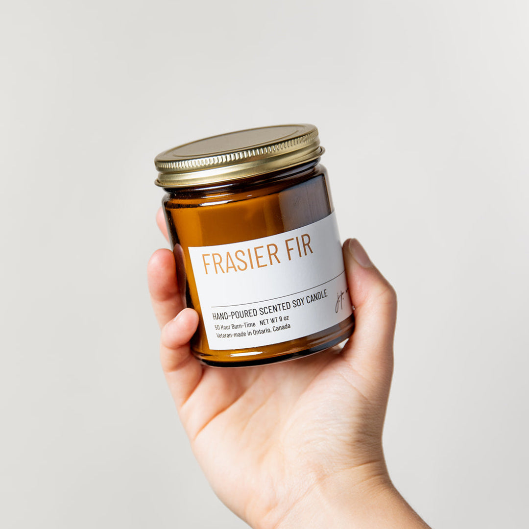 Hand holding a 'Frasier Fir' candle jar against a light background