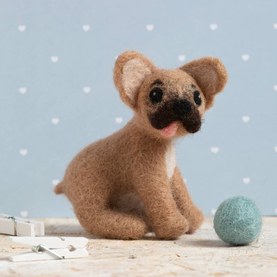 Small brown dog toy with a black nose on a light wooden surface against a light blue background with white polka dots.
