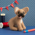 Felted animal toy on a blue surface with spools of thread and a polka dot background