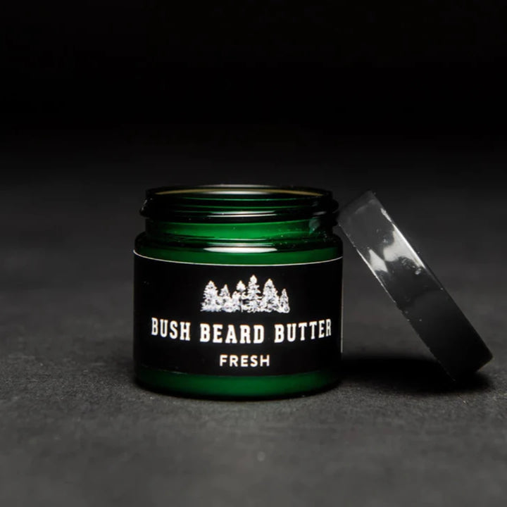 A dark green glass jar with a black lid. The jar is filled with beard butter and has a black label with the text 
