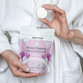 Person holding a Naturebee shower steamer and packaging in a white robe.