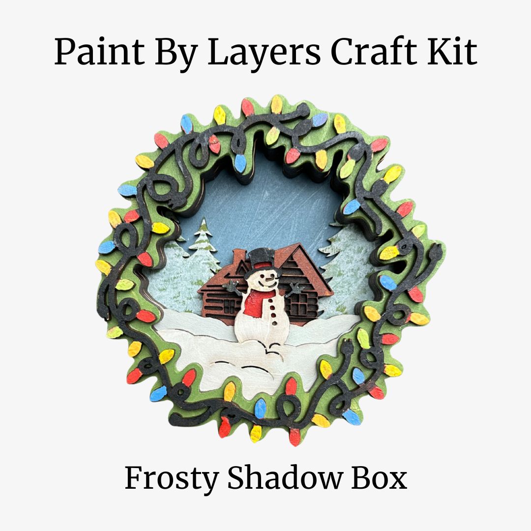 Paint by Layers Craft Kit for Frosty Shadow Box with a snowman and cabin design.